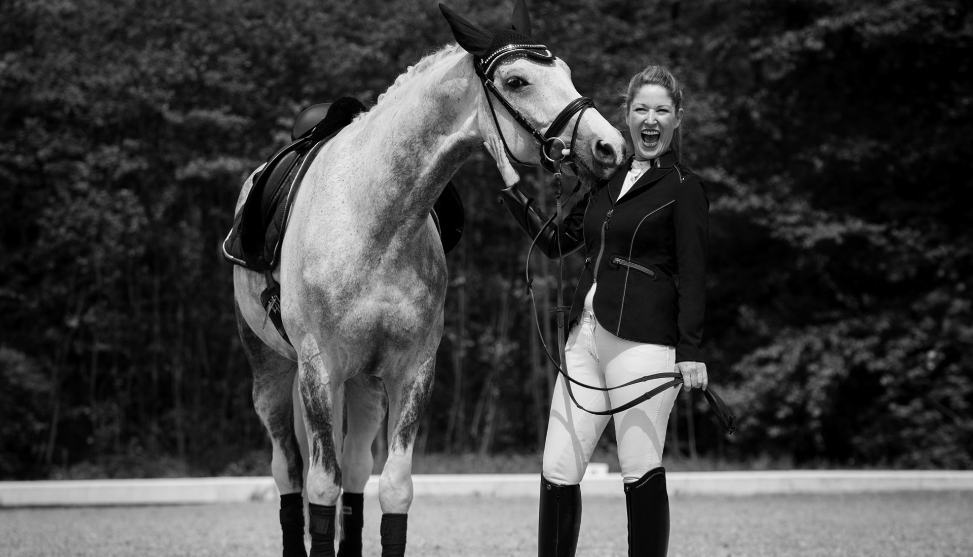Glückliche Frau mit Tunrnieroutfit und schönem Pferd am lachen
